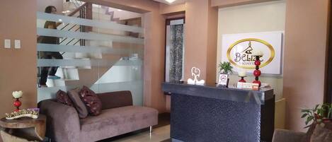 A modern reception area with a sofa, a reception desk, a ceiling fan, and a staircase.