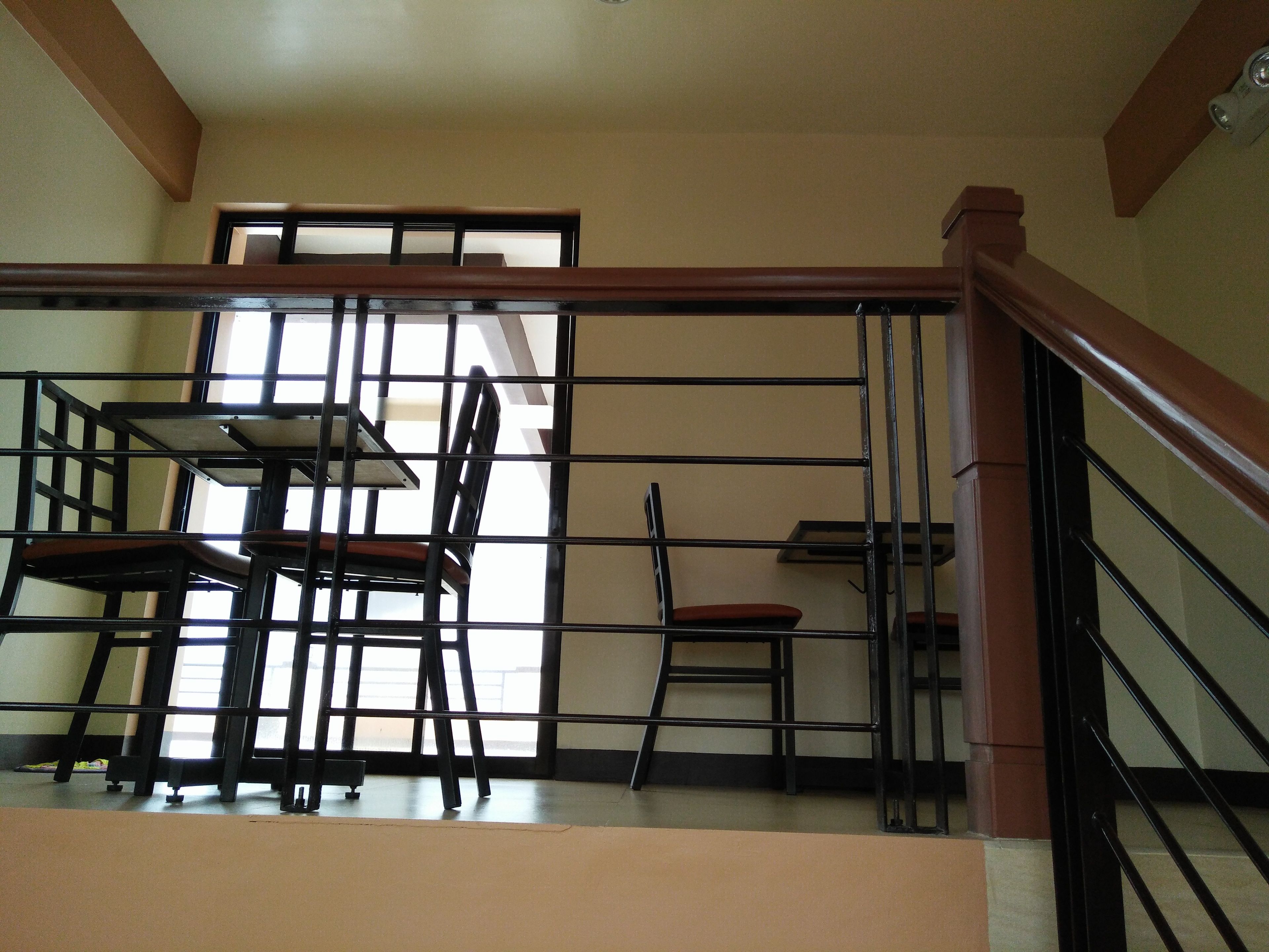 A staircase with a wooden handrail and metal railings, leading to a room with a table and chairs.