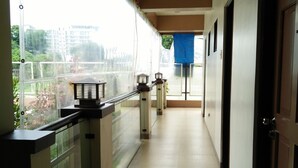 A corridor with a glass railing, a blue tarp over a door, and a view of buildings and greenery outside. - Belize Tagaytay (Tagaytay)