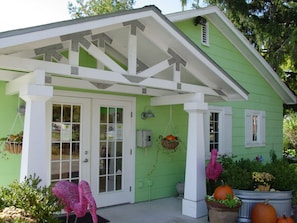 A green house with white trim, a porch with a white railing, and hanging flower baskets. - The Pines Motorlodge (Douglas)