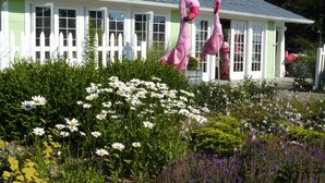A house with a white picket fence, surrounded by a garden with various flowers and plants. - The Pines Motorlodge (Douglas)