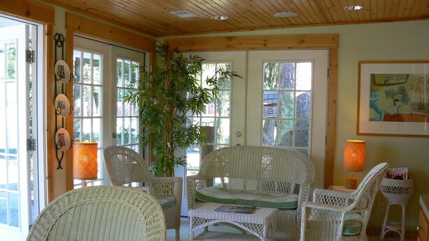 A room with wicker furniture, including chairs and a sofa, a large potted plant, and a framed picture on the wall. - The Pines Motorlodge (Douglas)