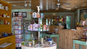 A room with a round table, shelves with books and decorative items, a wooden ceiling, and a poster on the wall. - The Pines Motorlodge (Douglas)