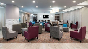 A hotel lobby with multiple seating areas, a flat-screen TV, and a patterned carpet. - La Quinta Inn & Suites by Wyndham Forsyth (Forsyth)