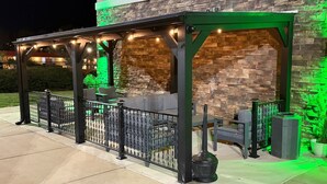 An outdoor patio with stone walls and green lighting, featuring seating and a pergola. - La Quinta Inn & Suites by Wyndham Forsyth (Forsyth)