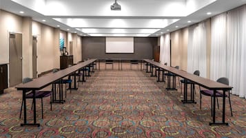A conference room with a long table, chairs, a projector screen, and a carpeted floor.