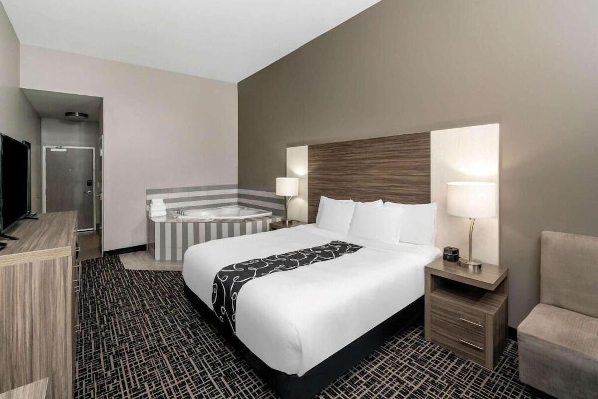 Une chambre d’hôtel comprenant un lit, des lampes de chevet, une petite table, une chaise, un téléviseur, une salle de bain avec baignoire et une douche.