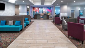 A hotel lobby with seating areas, a reception desk, and a colorful mural on the wall. - La Quinta Inn & Suites by Wyndham Forsyth (Forsyth)