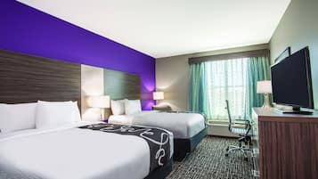 A hotel room with two beds, a desk, a television, and a window with curtains.
