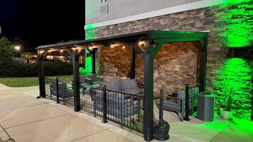 Un patio al aire libre con pared de piedra, iluminación verde y mobiliario exterior.
