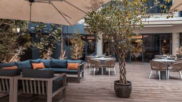 An outdoor patio area with a sofa set, dining tables, and a large potted tree.