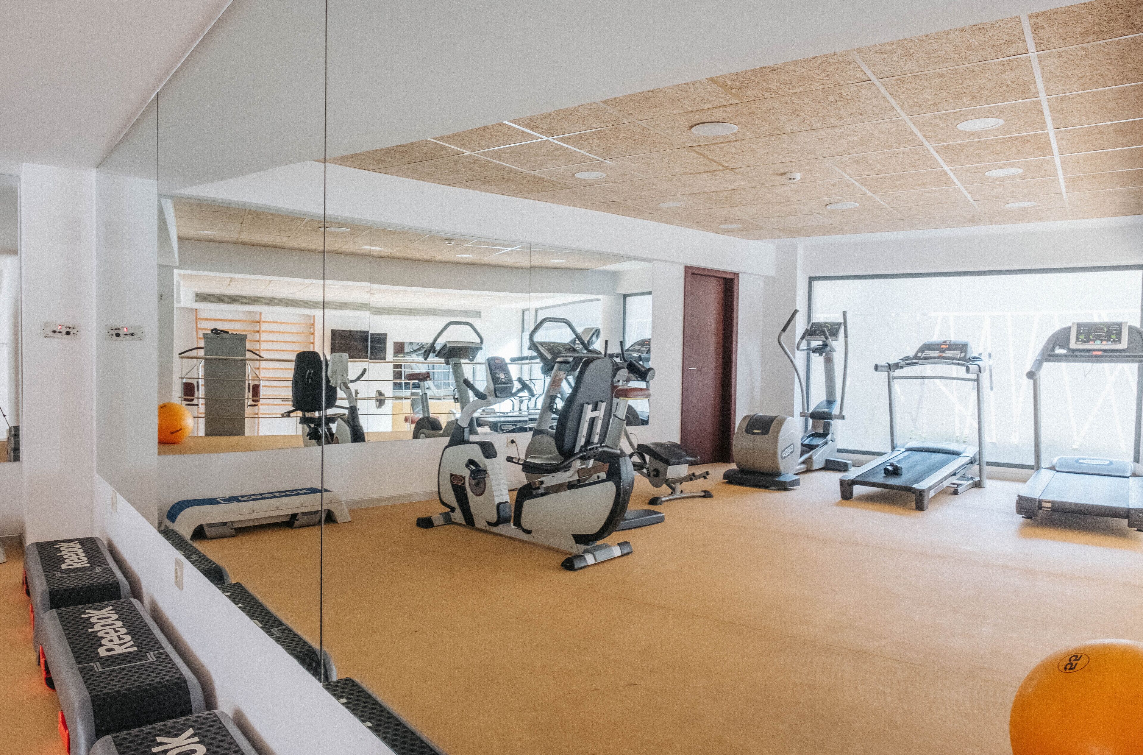 Un gimnasio con máquinas de cardio, un espejo grande y un ventanal.