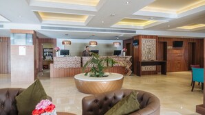 Um saguão de hotel com balcão de recepção, assentos de couro e uma planta decorativa.
