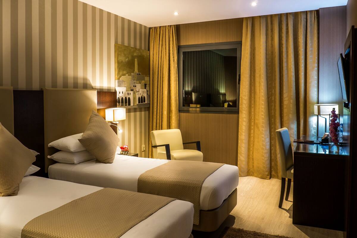 A hotel room with two beds, a chair, a desk, and a window with curtains.