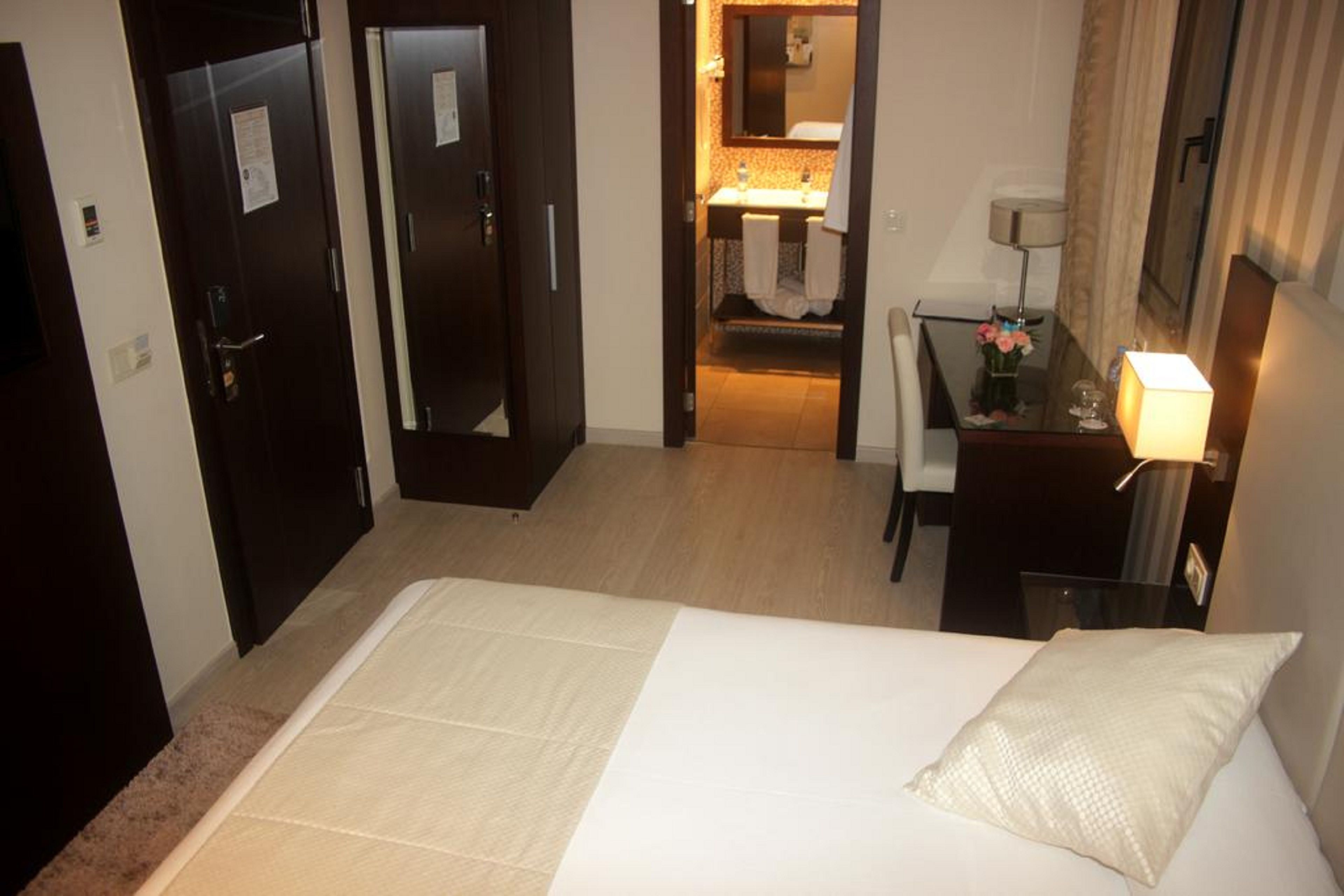 Una camera d'albergo con un letto, una scrivania, una lampada e un bagno visibile attraverso una porta aperta.