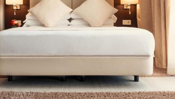 Uma cama grande com cabeceira, duas luminárias laterais e uma paleta de cores neutras.