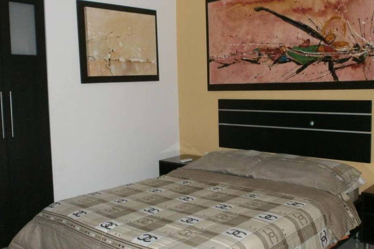 A bedroom with a bed, a nightstand, a dresser, and two framed artworks on the wall.