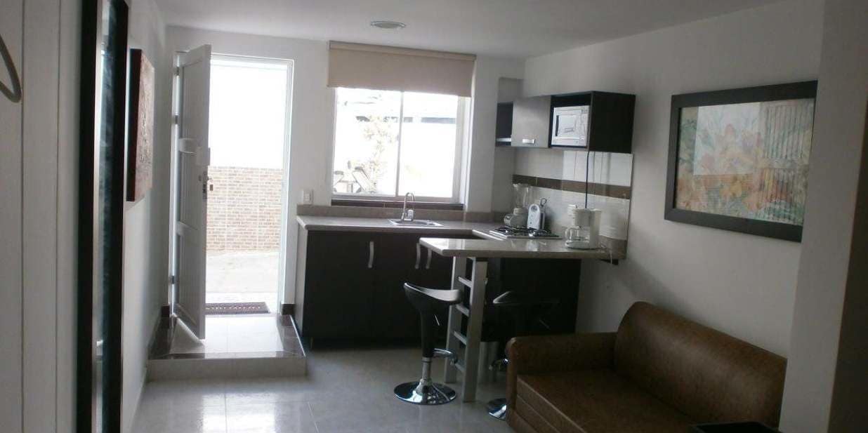 A compact kitchen with a dining area, a bar stool, and a brown sofa.