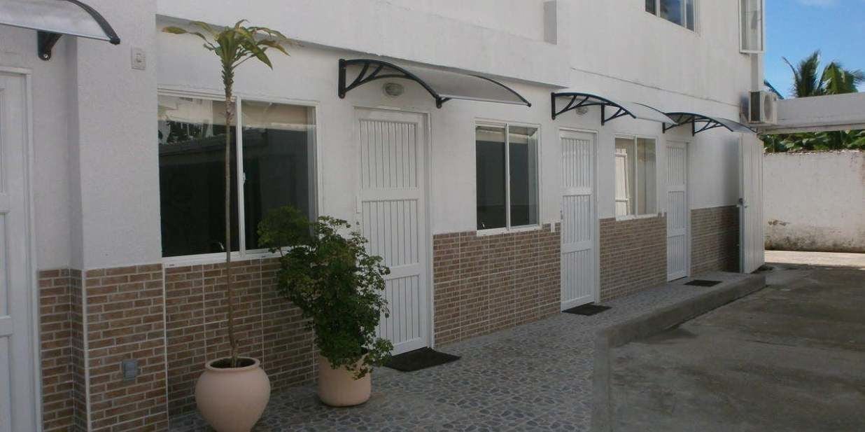 Um edifício com paredes externas brancas, seção inferior em tijolos e várias janelas com persianas brancas.
