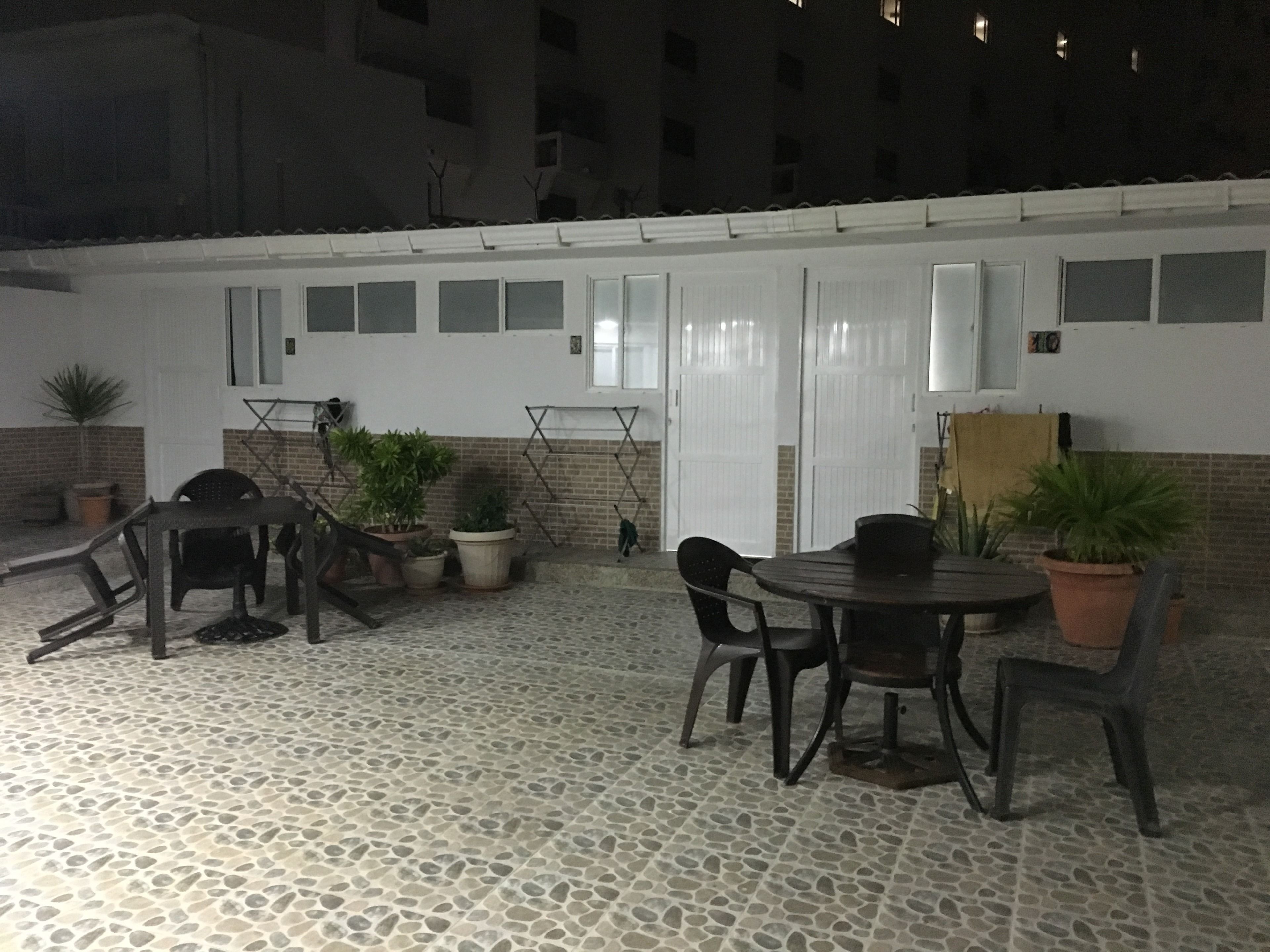 Ένας εξωτερικός χώρος με τραπεζάκι και καρέκλες, διακοσμημένος με φυτά σε γλάστρες και με έναν τοίχο από τούβλα.