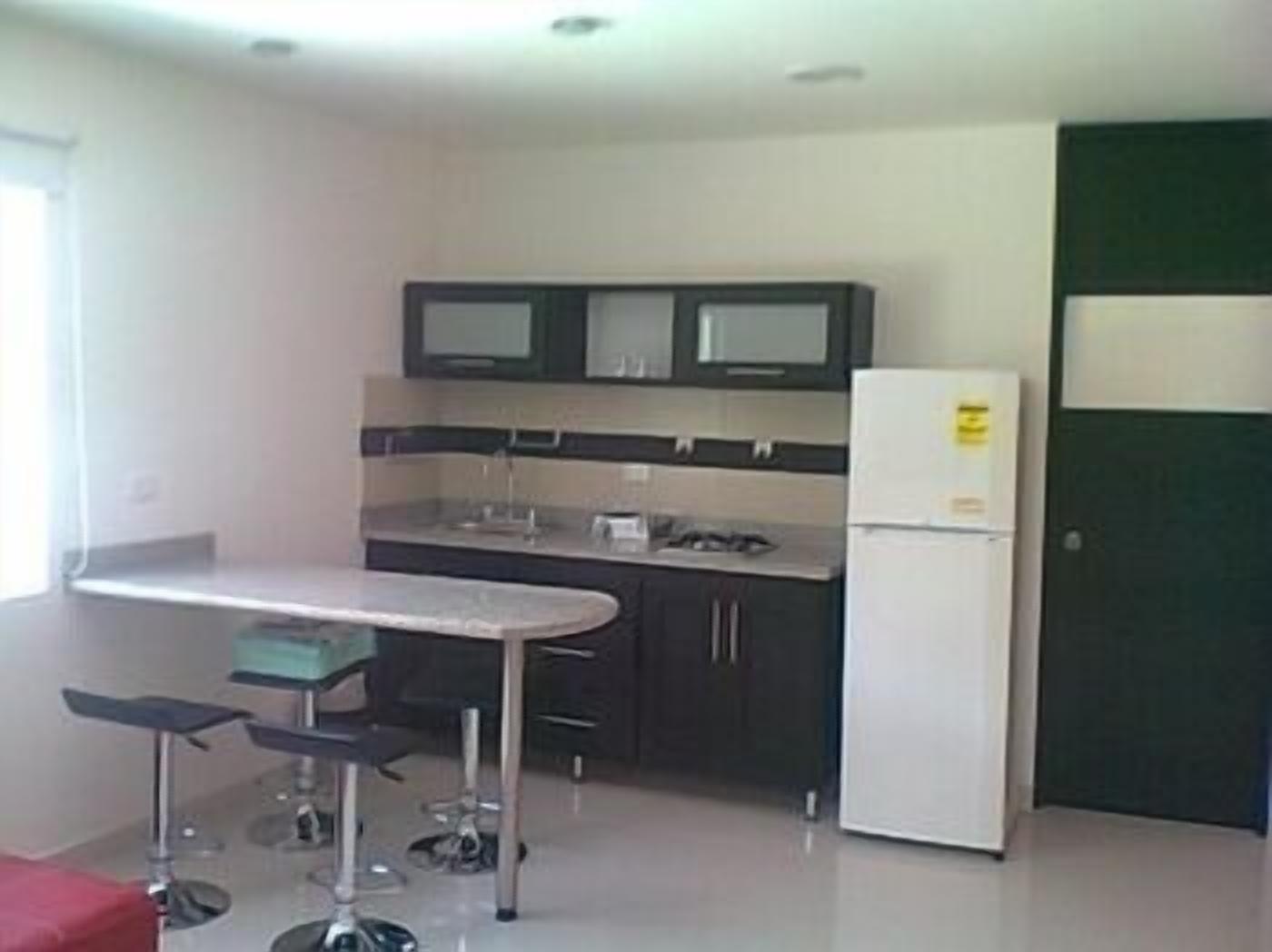 A compact kitchen with dark cabinets, a white refrigerator, and a small bar area with stools.