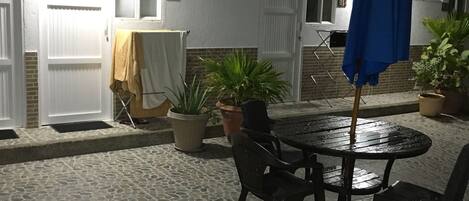 An outdoor patio with a round table and chairs, potted plants, and a blue umbrella.