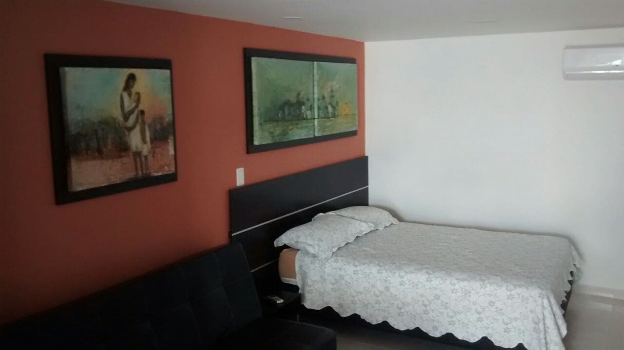 Een slaapkamer met een bed, nachtkastje en twee schilderijen aan de muur.