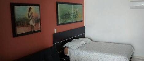 Een slaapkamer met een bed, nachtkastje en twee schilderijen aan de muur.