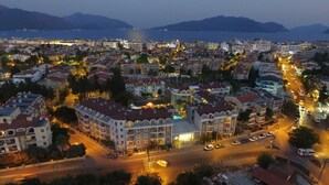 An aerial view of a cityscape at dusk with buildings, roads, and a body of water in the background.