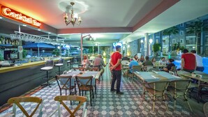 A restaurant with a bar area, tables, chairs, and a neon sign.