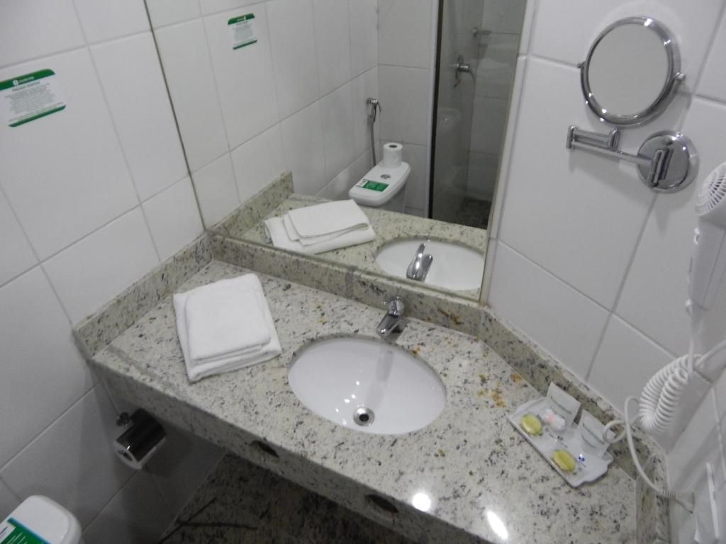 A bathroom with a granite countertop sink, a mirror, a toilet, and a hand dryer.