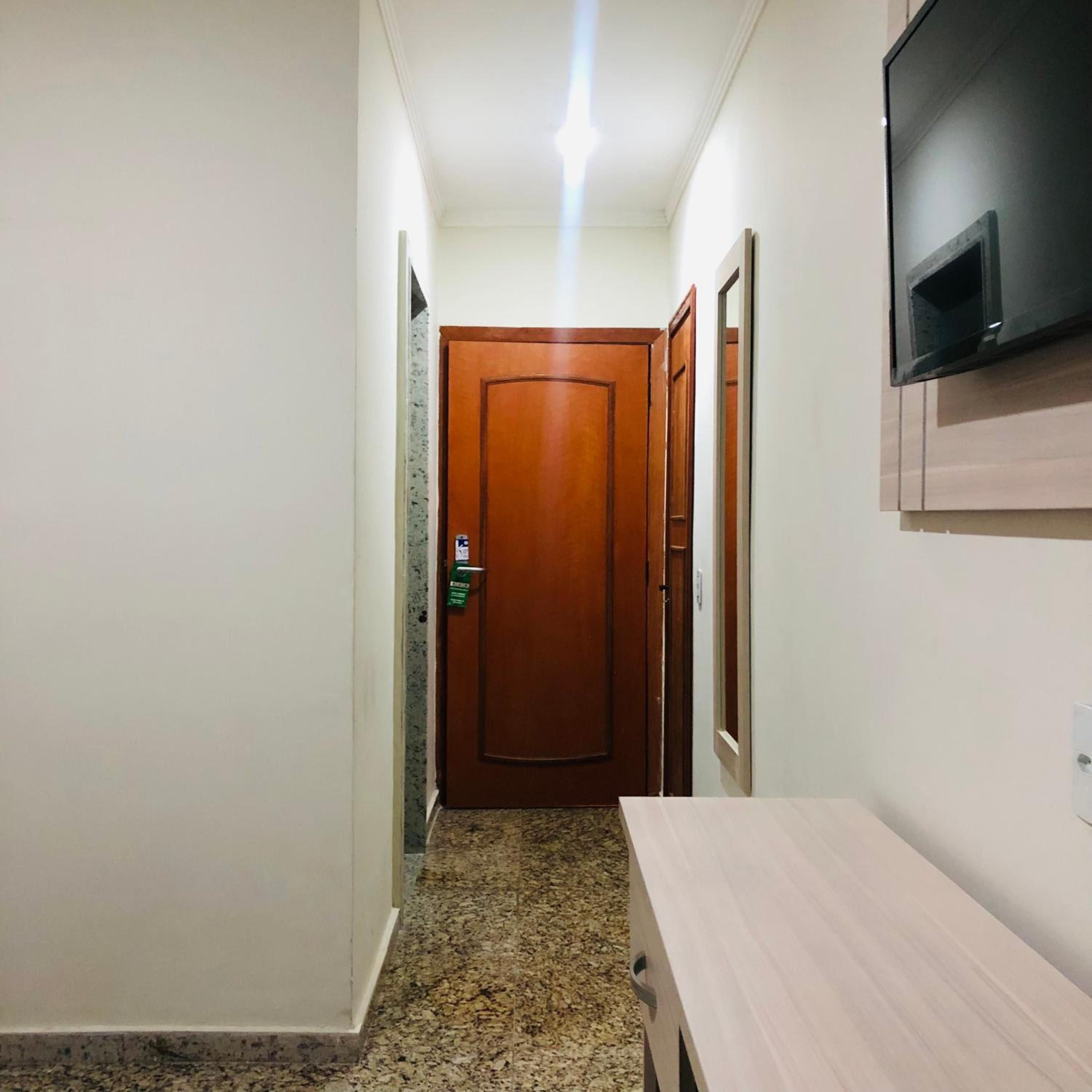 A hallway with a wooden door, a television mounted on the wall, and a wooden table.