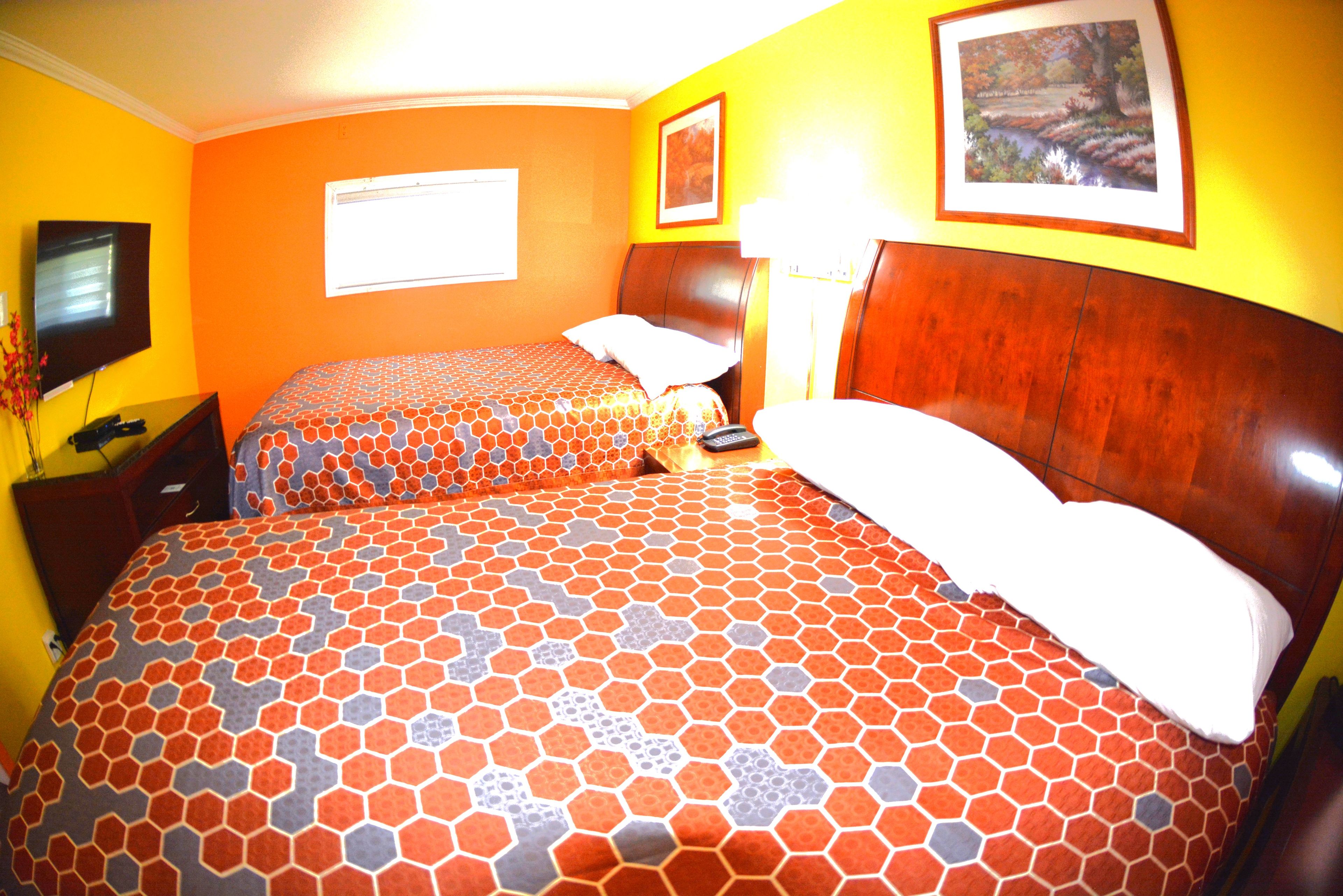 A hotel room with two beds, a TV, a desk, and a lamp.