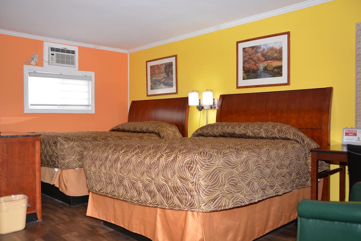 A hotel room with two beds, a window, an air conditioning unit, and two framed pictures on the wall.