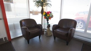 Deux fauteuils en cuir marron, placés face à face dans une pièce dont le sol est recouvert de carreaux, avec une table basse en verre et un vase rempli de fleurs.