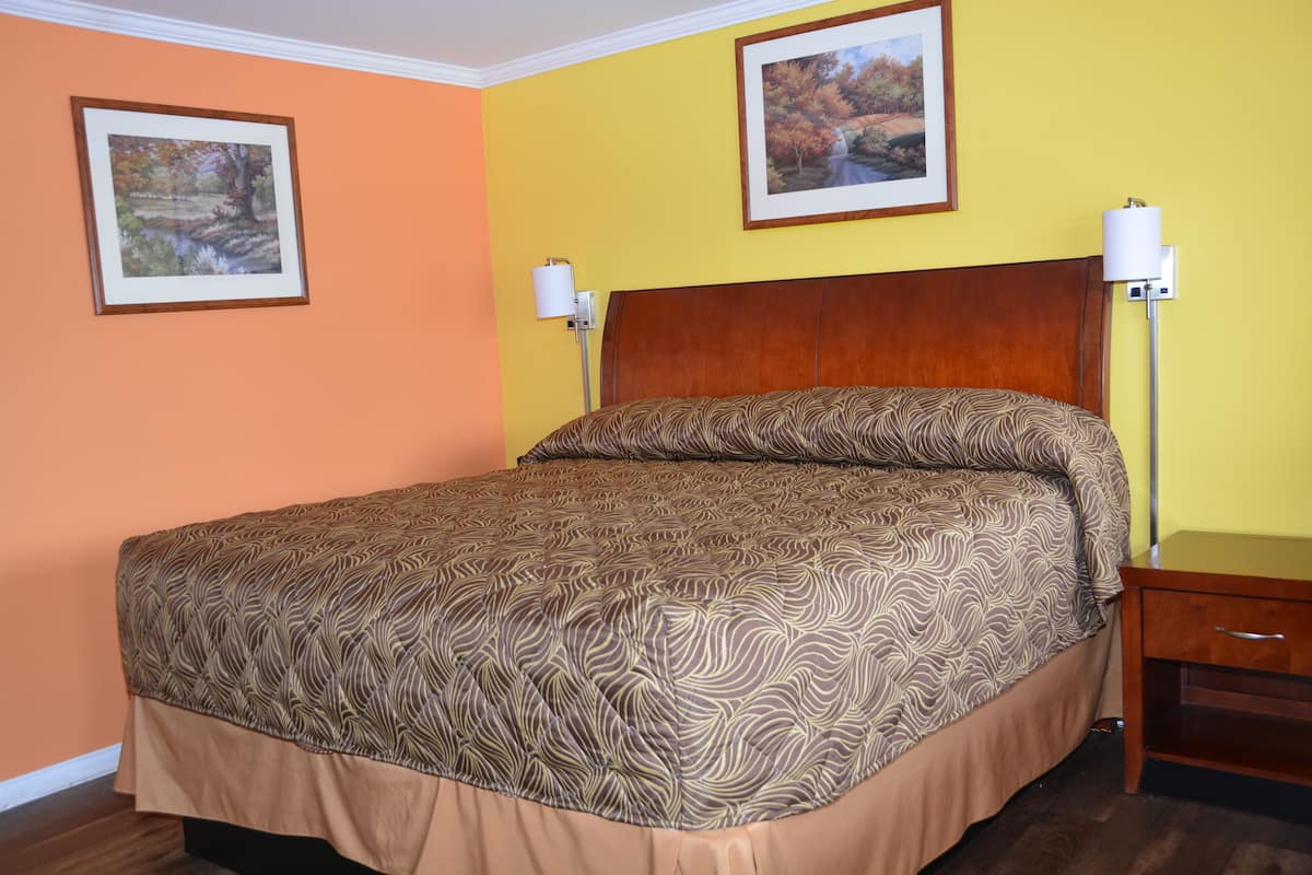 A hotel room with a large bed, two framed pictures on the walls, and a nightstand with a lamp.
