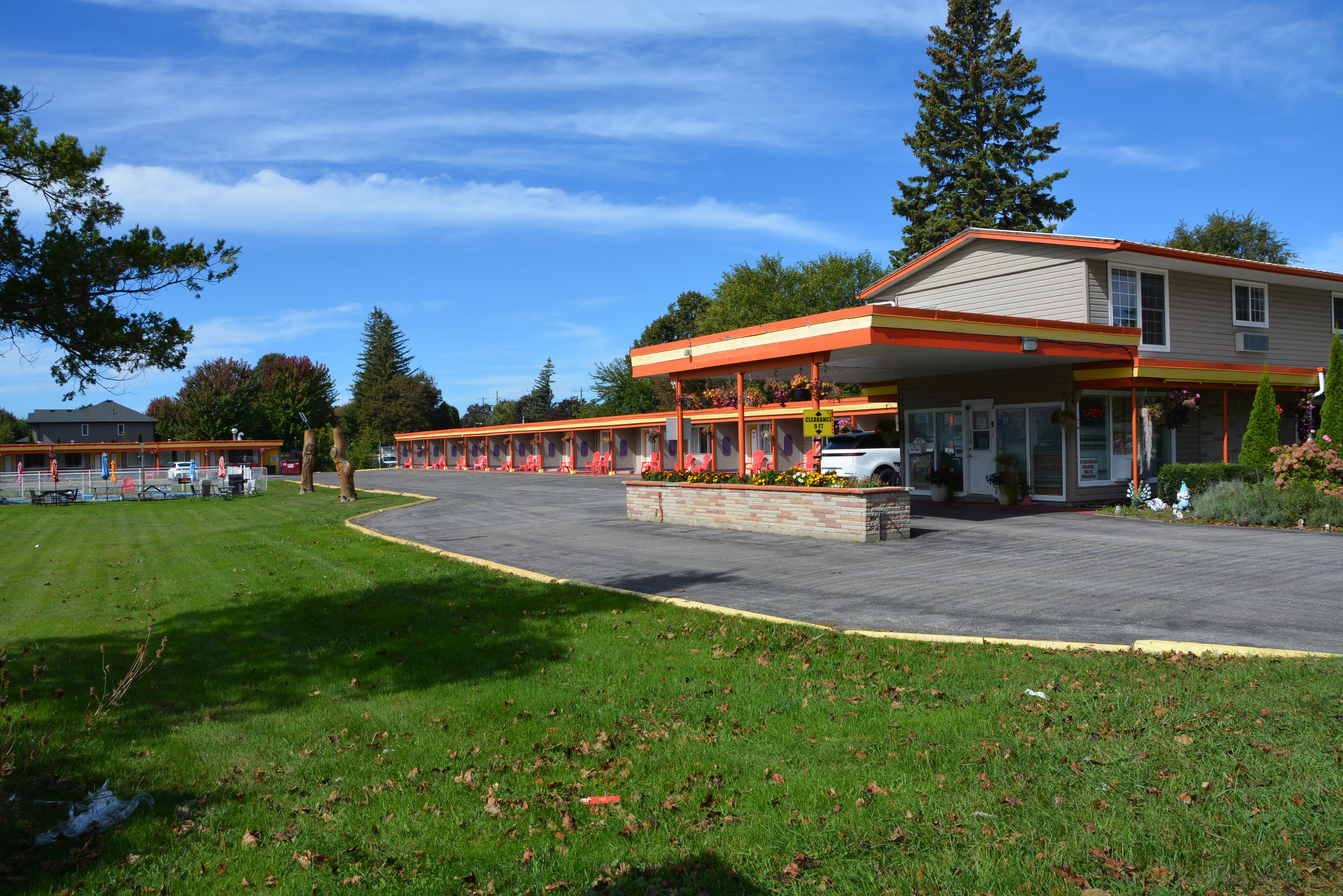 Un motel doté d’un parking, d’un espace extérieur abrité avec des sièges et d’un bâtiment à la façade rouge et blanche.