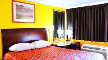 A hotel room with a large bed, a bedside table with a lamp, a telephone, and an air conditioning unit.