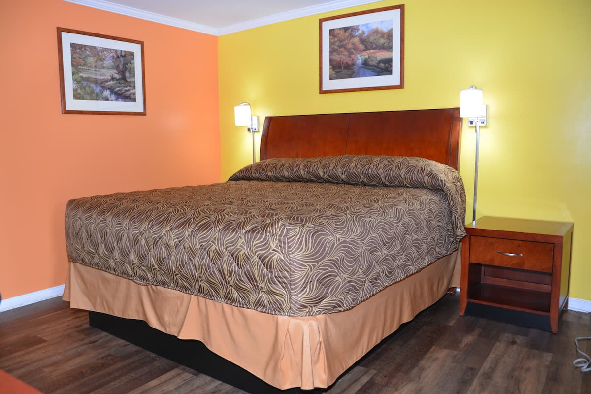 A neatly made bed with a patterned bedspread and a wooden headboard. There are two wall-mounted lamps on either side of the bed.