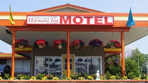 Motel Harmony Inn con un letrero llamativo, un acceso cubierto, cestas de flores colgantes y una estatua al frente.