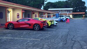 Un estacionamiento con tres coches deportivos, un bote y un edificio de techo rojo.