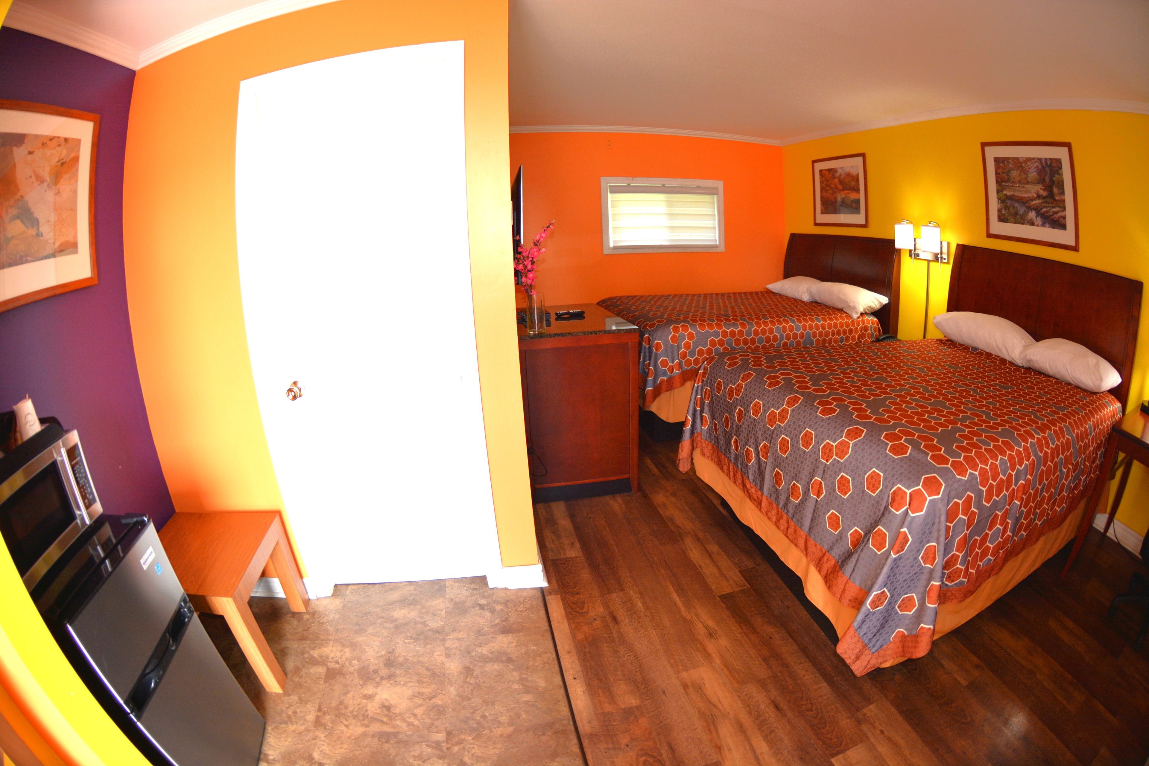 A hotel room with two beds, a desk, a chair, a microwave, and a door.
