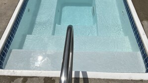 Une piscine rectangulaire à l’eau d’un bleu limpide, avec un escalier en métal et un bord carrelé.