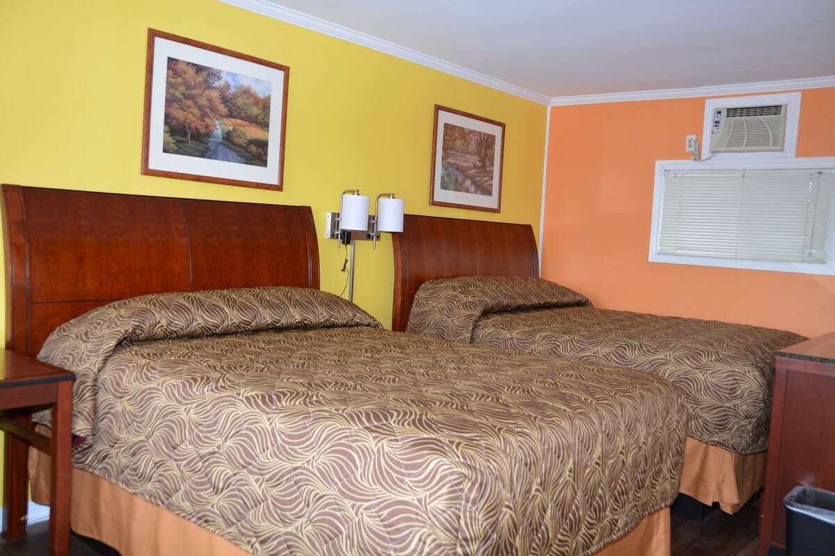 A hotel room with two beds, wooden headboards, and two wall-mounted lamps.