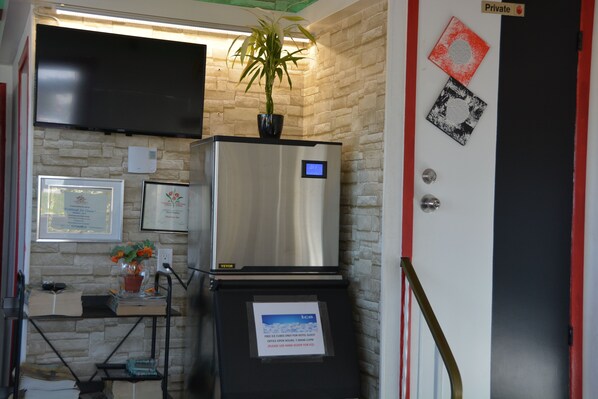 Una kitchenette compacta con refrigerador, una mesita con una planta en maceta y un televisor instalado en la pared.