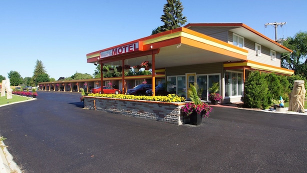 Un motel Harmony Inn doté d’un porche avant couvert, d’un parking et d’une rangée de chambres de motel en arrière-plan.