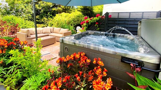 Un jacuzzi rodeado de vegetación exuberante y un sofá exterior color beige.