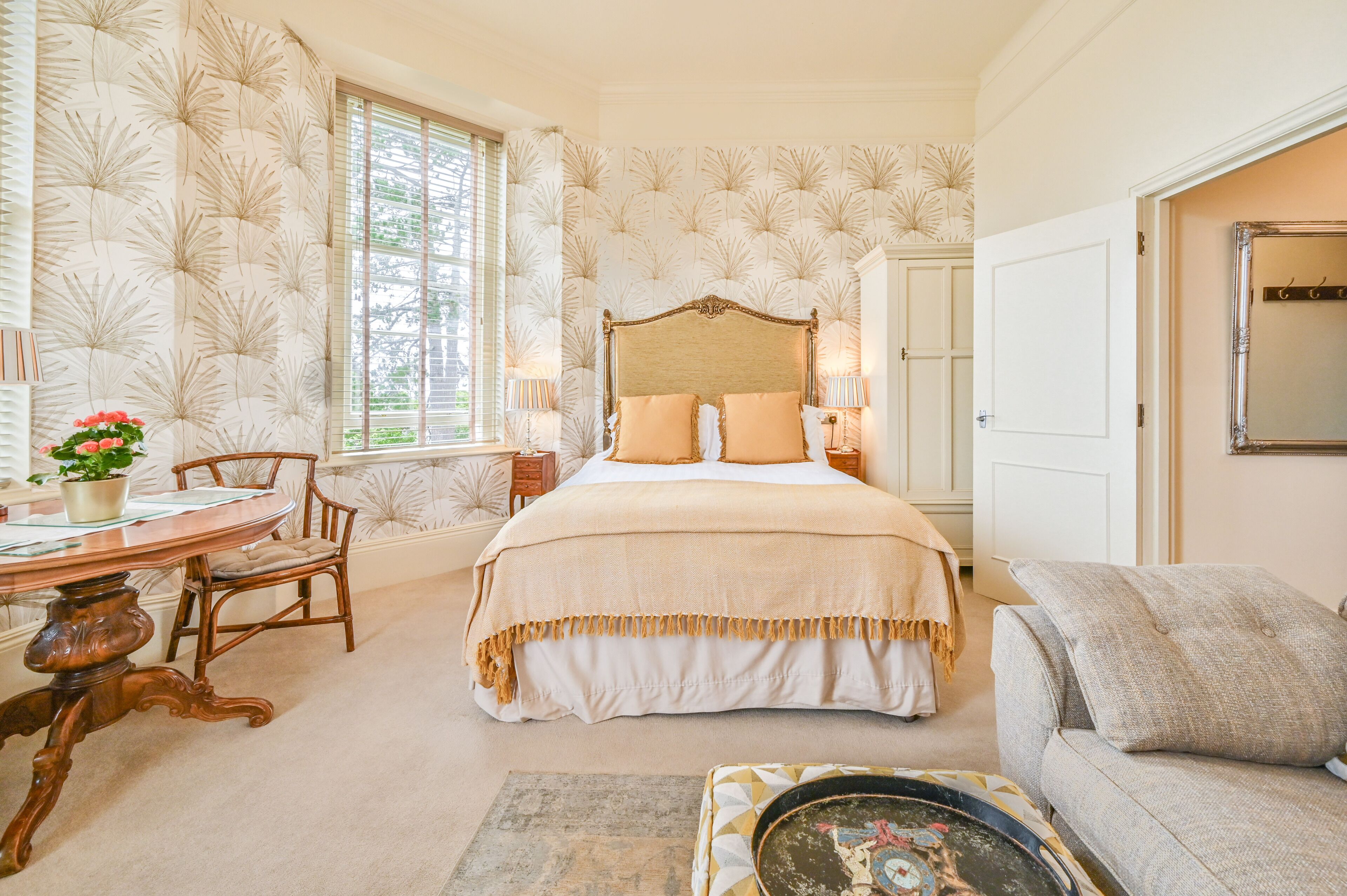 A bedroom with a large bed, a dining table with chairs, a sofa, and a decorative mirror.