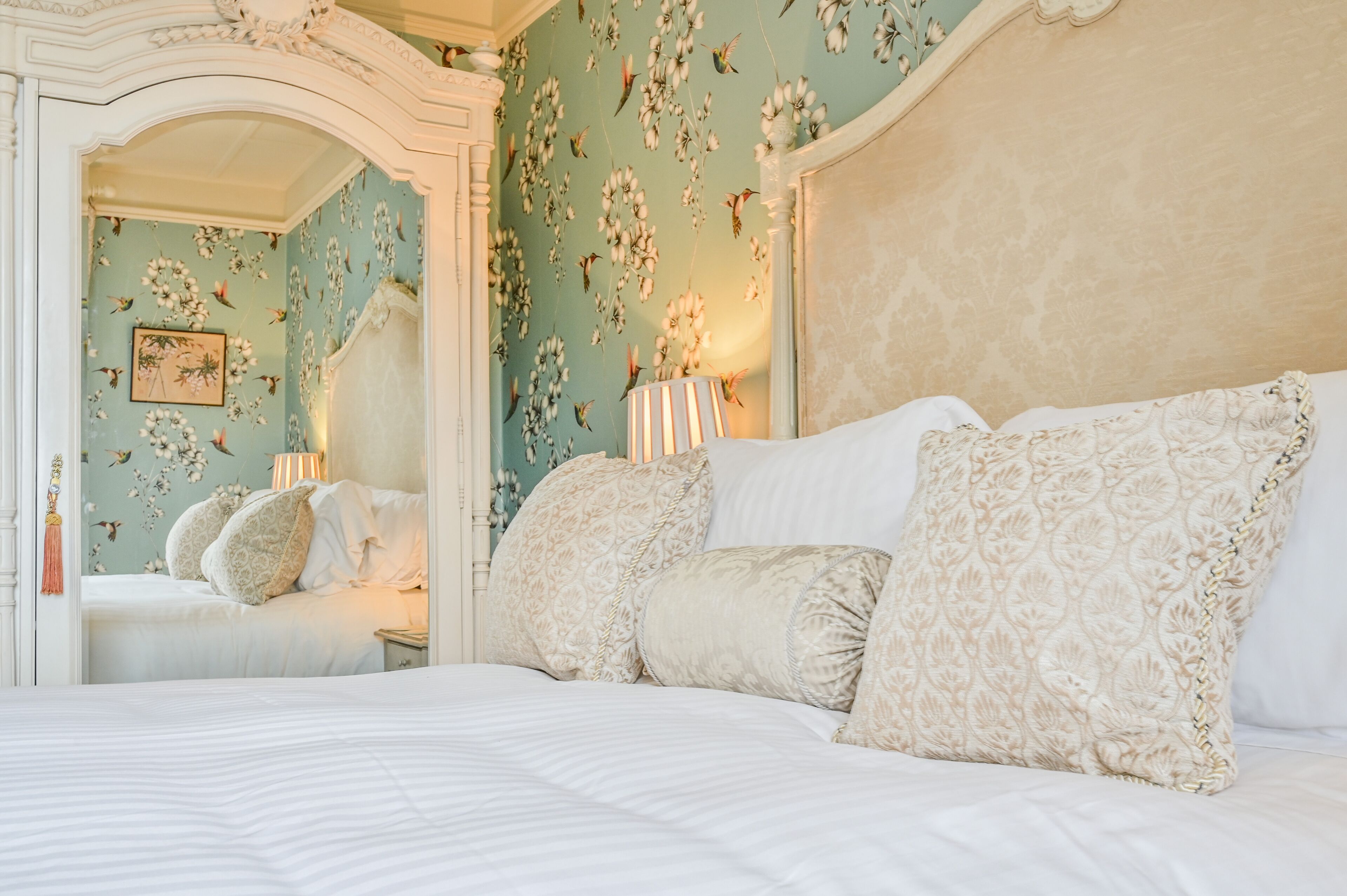 Une chambre à coucher avec un grand lit, un papier peint à motifs floraux et une tête de lit décorative.