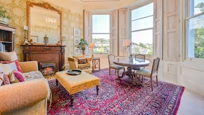 Una habitación tradicional con chimenea, un espejo grande, una mesa de comedor con sillas y vistas a través de un ventanal.